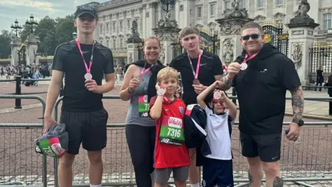 Damien Knowles A family hold up medals in front of Buckingham Palace