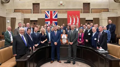 Reform UK A group of Reform UK councillors standing in a semi-circle in a council chamber.