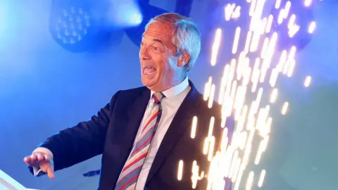 Getty Images Celebrating onstage, Nigel Farage smiles as sparks fly from pyrotechnics on his left