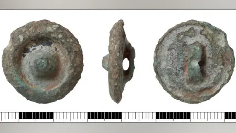 Three views of a late Bronze Age round button. The first image on the left shows its front face, which has a large conical central boss within a broad, deep concave depression, surrounded by a thick convex rim that slopes down to the edge. The middle image shows it on its side revealing its attachment loop. The third image on the right shows its reverse with the attachment loop in the middle.
