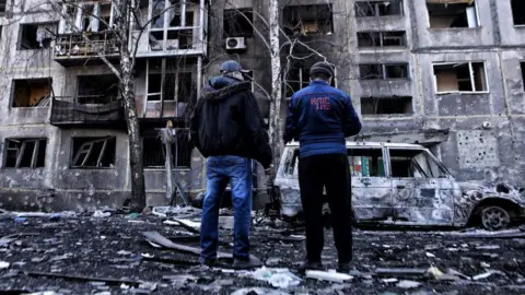 Two men look at damaged apartment block in Dobropillya, Ukraine