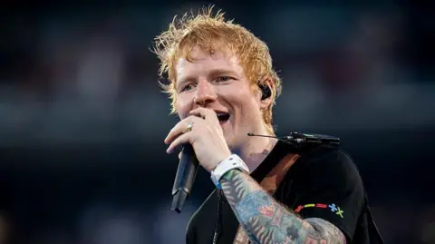Ed Sheeran singing at a concert in Madrid. He is wearing a black T-shirt.