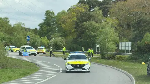 Police cars and officers on a slip road. There is a 'police slow' sign in the road.
