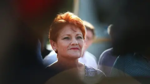 Getty Images Pauline Hanson – wearing bright red hair and red lipstick – smiling off into the distance.