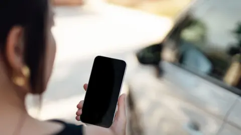 Mujer de embarcadero sosteniendo un teléfono junto al coche