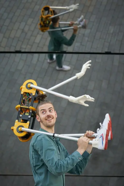 Freedom Festival A man wearing a green shirt smiles as he holds a bizarre-looking robotic device which has fake hands and feet attached to a black and yellow motor