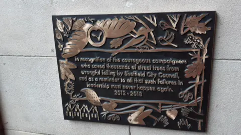 Julia Armstrong/LDRS A black plaque with brass-coloured writing on, which says: "In recognition of the courageous campaigners who saved thousands of street trees from wrongful felling by Sheffield City Council, and as a reminder to all that such failures in leadership must never happen again. 2012-2018."