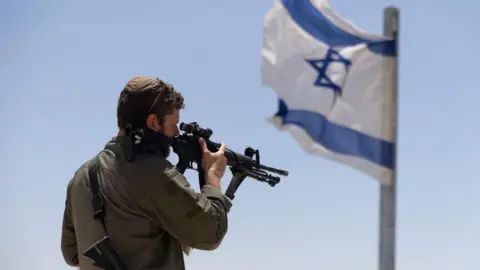 Getty Images An soldier with a gun stands near an Israeli flag