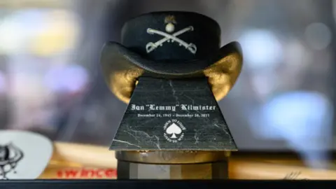 Getty Images An urn with a cowbot hat perched on top opf it. The hat displays a logo of two crossed swords, and the urn, which is black, displays the words Ian 'Lemmy' Kilmister and the dated December 24 1945 to December 28 2015