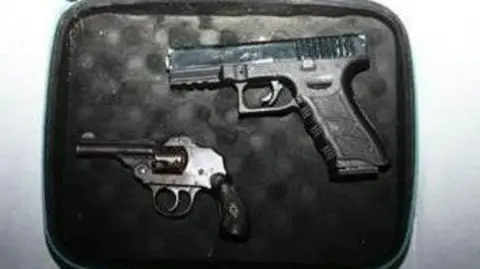 Two guns - a Glock-style pistol and a revolver - lie in a small case which has black padding.