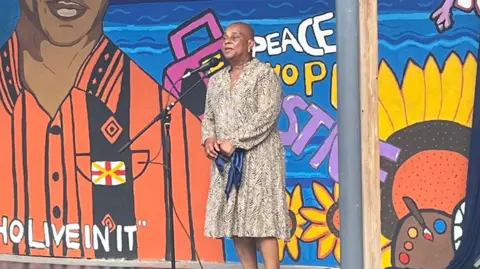 Baroness Lawrence speaks into a microphone in front of the mural