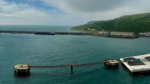 An aerial view of Portland Port. The sea is blue and there is a harbour wall in the background.