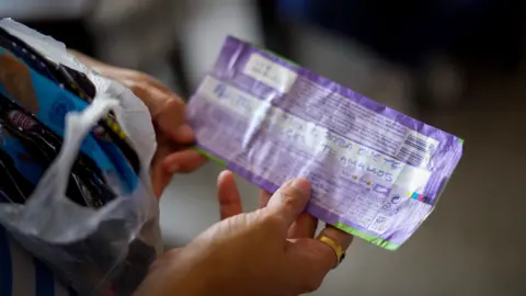 BBC A person holds a chocolate bar wrapper in their hands with words written on it in blue ink 