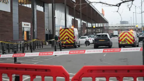 Ambulances and emergency cars parked outside the Marks and Spencer building with a red and white police tape.