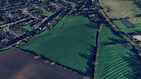 Google Earth An aerial view of a field from above, with houses to the left of the image