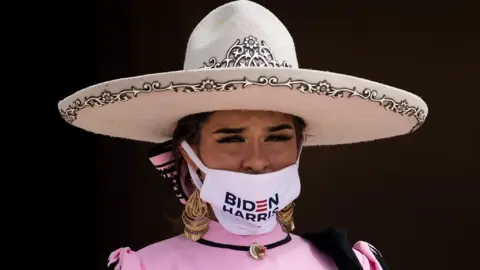 Getty Images A woman wears a hat and a mask that reads "Biden Harris"