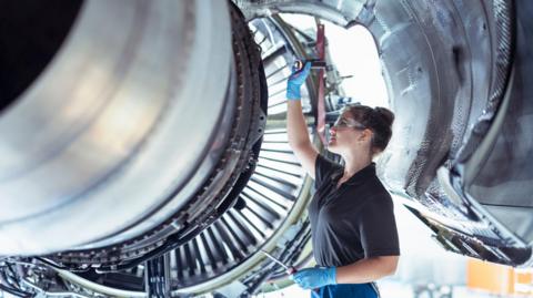 A female apprentice works on a jet engine
