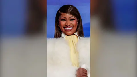 A woman, Nicki Minaj, smiling wearing a fluffy white jacket.