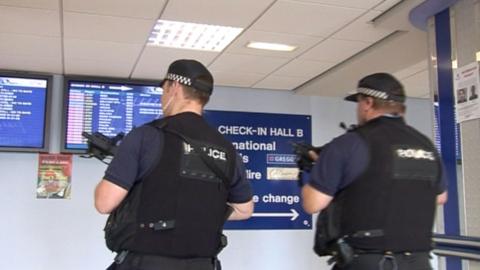 Two police officers holding guns in an airport.