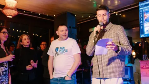 Kelsie Scully Photography Professor Rob Galloway standing alongside Brighton & Hove Albion manager Fabian Hurzeler who is speaking on a microphone and addressing a crowd