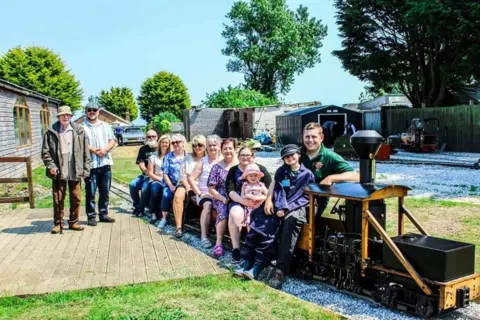 A group of people are sitting on a ride-on model railway