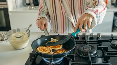 Woman cooking pancakes in a frying pan on a gas hob