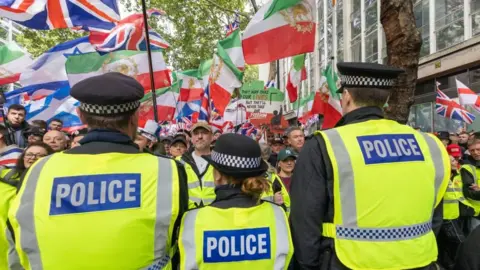 EPA/Shutterstock Rear view of three police officers with crowd waving a selection of flags before them