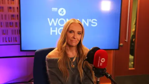 A woman, Toni Collette, sits in the Woman's Hour radio studio behind a microphone