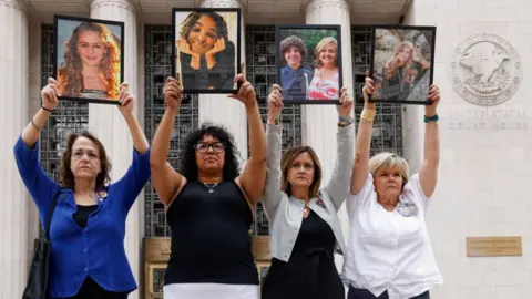 Four parents holding up framed photos of their children, whom they say died due to social media–related harms standing alongside one another outside a courthouse in Los Angeles.
