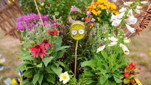 PA Media A bee made out of an old tin and recycled materials sits in a planting box filled with brightly coloured flowers.