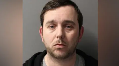 Met Police Police custody image of Durkan. He has short, dark hair and looks into the camera.