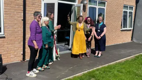 LDRS The Mayor of Worcester wearing a yellow dress and green jacket holds up a pair of scissors.