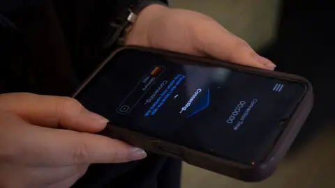 NurPhoto / Getty Images A woman holds a phone that shows a screen which says the word "connecting" on it