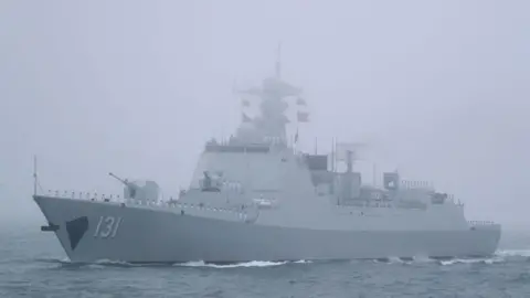 Getty Images A large navy ship flying Chinese flags sails on misty ocean