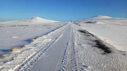 DOI A road covered in snow, between two peaks of hills.