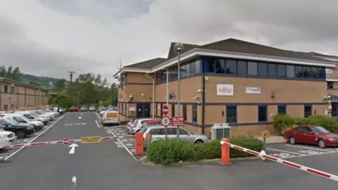 Brown brick office building with car park and barrier in front