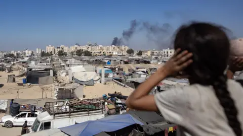 EPA A Palestinian girl covers her ears as Israeli air strikes hit residential buildings  close to tents for displaced people in Khan Younis, in the southern Gaza Strip (16 August 2024)