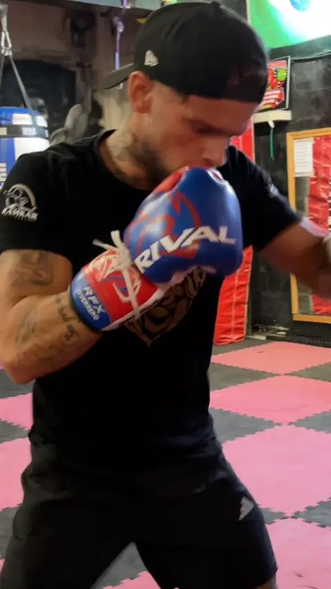 A man with boxing gloves on mid punching a punching bag. 
