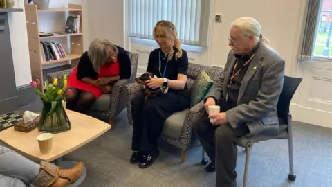 BBC/Louise Fewster Dachshund sat on her owner's knee looking towards a volunteer