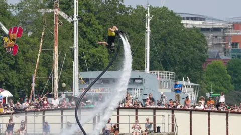 Plaster/Bristol Harbour Festival A man is doing a flip over the water while on a flyboard above water.