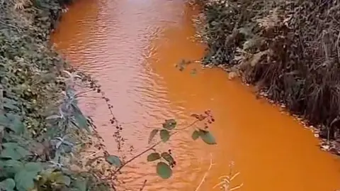 The Dark Side Of The Moor Water in the River Calder at Todmorden which is heavily discoloured making it appear to be orange