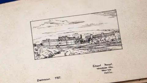 A pen and ink drawing of Dartmoor Prison on a yellowing page in the album. It includes the caption Dartmoor 1917