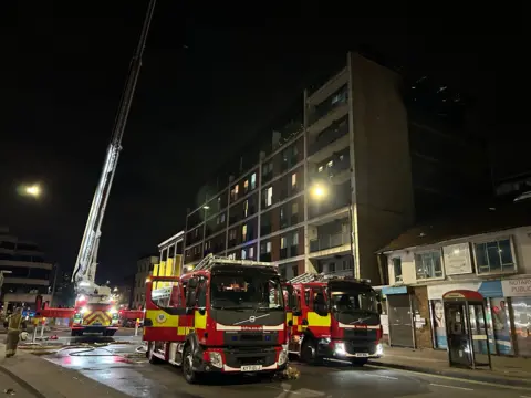 Slough Borough Council Three fire engines outside the Mosaic Apartments building Slough, with a tall platform elevated from a fire engine on the left of it 