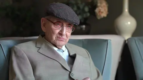 An elderly man in smart clothes and hat.