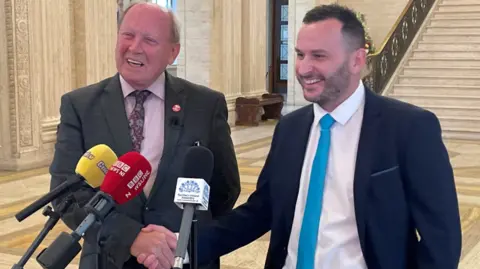 PA Media Jim Allister and Timothy Gaston smile and shake hands in the great Hall of Stormont