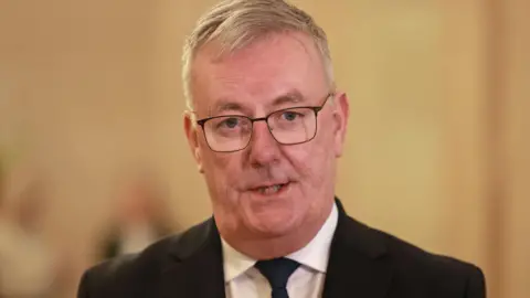 PA Media Mike Nesbitt - He has grey hair and is wearing a black suit, black tie and white shirt and black-rimmed glasses which are rectangular in shape.