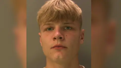 A police custody image of Rhys Hedges who is looking at the camera and has blond hair. Only his head is in shot.