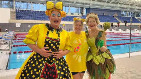 Sam Rabone from pantomime Jack & The Beanstalk is in a yellow costume on the left with Gill Jordan, better known as Doreen Tipton, on the right also dressed up, in green. Swimmer Kath Stanczyszyn is wearing a yellow t-shirt in the middle.