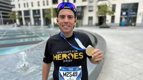 Ricardo Sousa Ricardo smiles at the camera with his medal around his neck and he is wearing a Holidays for Heroes Jersey running top
