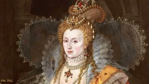 Nicole Ryder The Rainbow Portrait of Elizabeth I showing her wearing pearls in her red hair. She is wearing three ruffs, one outspread like wings around her head and shoulders, the other raised lace around her neck, the third under her chin. She is wearing ropes of pearls and her dress is yellow.